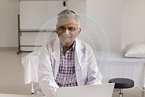 Cheerful elder Indian doctor man wearing white coat and glasses