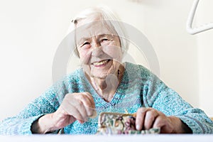 Cheerful elderly 96 years old woman sitting at table at home happy with her pension savings in her wallet after paying