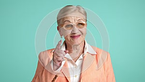Cheerful elderly blonde woman in stylish glasses winking, pointing index finger