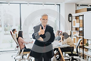 A cheerful elderly businessman stands smiling, giving a thumbs-up with a team of professionals working in the background