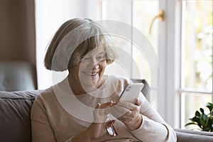 Cheerful elderly great grandma woman using mobile phone at home