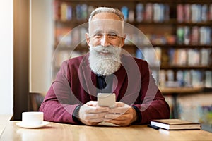 Cheerful elderly grey-haired man using mobile phone at cafe