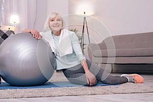 Cheerful elderly lady posing while leaning on yoga ball