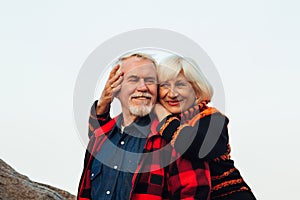 Cheerful elderly people a woman and a man are sitting on the stones and hugging on the lake, against the background of the bridge