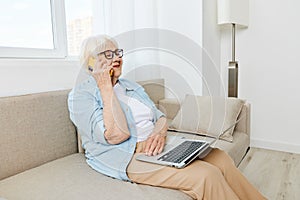 a cheerful elderly woman in glasses and a light shirt talking on the phone is working at a laptop enjoying the benefits