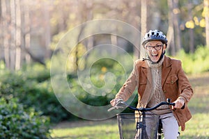 Cheerful elderly woman riding bicycle in public park. Activities for older people