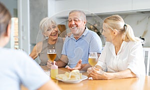 Cheerful elderly women and man gathering around kitchen table