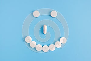 Cheerful emoticon from medical pills on a blue background. The concept of prevention of viral diseases