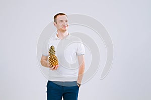 Cheerful and emotional guy holding a pineapple in his hand on a white background