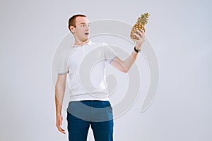 Cheerful and emotional guy holding a pineapple in his hand on a white background