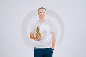 Cheerful and emotional guy holding a pineapple in his hand on a white background