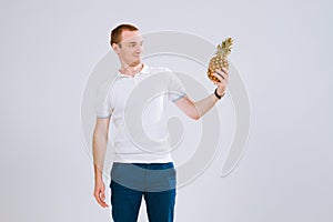 Cheerful and emotional guy holding a pineapple in his hand on a white background