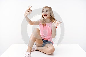 Cheerful enthusiastic happy blond teenage girl sitting crossed legs on floor, hold smartphone, record blog, communicate