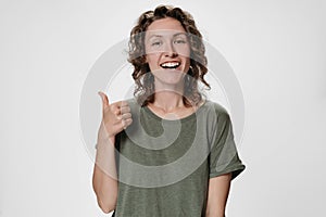 Cheerful enthusiastic pleased young caucasian curly woman showing thumbs up gesture