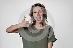 Cheerful enthusiastic young curly woman with opens eyes and mouth widely showing