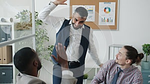 Cheerful entrepreneur working with laptop then dancing doing high-five with colleagues celebrating success