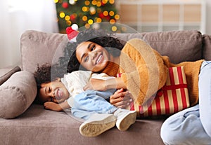 Cheerful ethnic family: happy child and mother congratulate each other at Christmas, playing and laughing