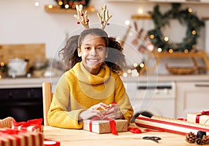 Cheerful ethnic girl decorating gift box on Christmas day