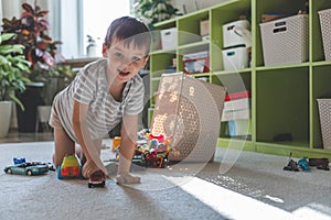A cheerful European boy plays with cars on the carpet in his room. The child dumped the toys