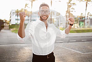 Cheerful european businessman raising hands up and rejoicing to victory outdoors on street, smiling at camera