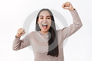 Cheerful excited asian girl rooting for football team, raising hands up, fist pump and smiling, shout from adoration and photo