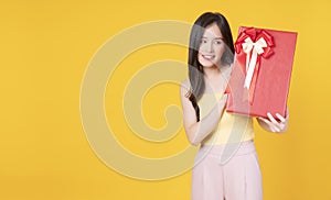 Cheerful excited asian woman holding red gift box with ribbon in own hand while standing over isolated blue background. Surprise