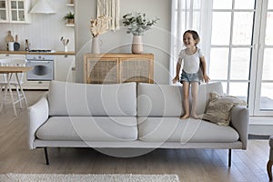 Cheerful excited little kid jumping on couch at home