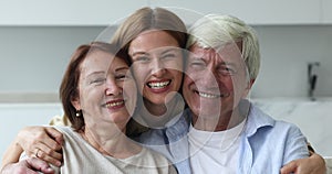 Cheerful excited loving adult daughter hugging couple of senior parents