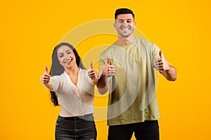 Cheerful excited young arabic couple in casual showing thumbs up sign with hands, recommend sale