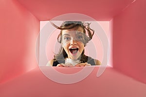 Cheerful and excited young girl looking inside carton box. Looking extremely happy
