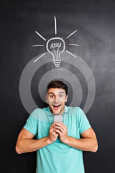 Cheerful excited young man holding smartphone and having an idea