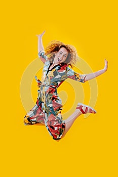 Cheerful exhilarated woman jumping in the air over yellow