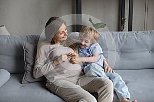 Cheerful expecting mom and little son hugging, relaxing on couch