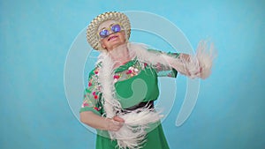 Cheerful expressive energetic old woman in a hat and boa dancing on a blue background