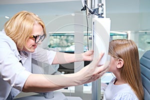 Cheerful eye doctor preparing little girl for binocular vision test photo