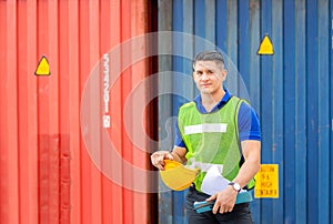 Cheerful factory worker holding hard hat, smiling man looking at camera with blurred container box background