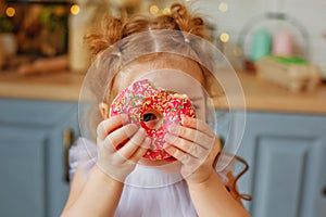 A cheerful family on the background of a bright kitchen. Daughter girl have fun with colorful donuts. He looks through the hole in