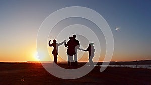 Cheerful family dances on shore of lake. Family weekend in park. Silhouettes sunset.