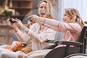 cheerful family with disabled child in wheelchair playing with joysticks together