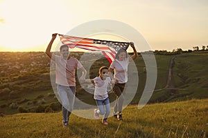 Cheerful family is having fun running along the grass in a summer park. USA July 4th Celebration.