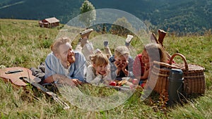 Cheerful family lying grass enjoying picnic on meadow. Summer holiday together.