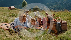 Cheerful family lying grass enjoying picnic on meadow. Summer holiday together.