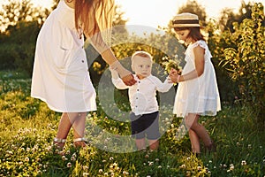Cheerful family of mother, little son and daughter spending free time on the field at sunny day time of summer