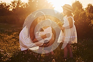 Cheerful family of mother, little son and daughter spending free time on the field at sunny day time of summer