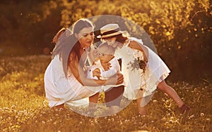 Cheerful family of mother, little son and daughter spending free time on the field at sunny day time of summer