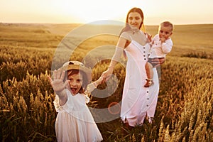 Cheerful family of mother, little son and daughter spending free time on the field at sunny day time of summer