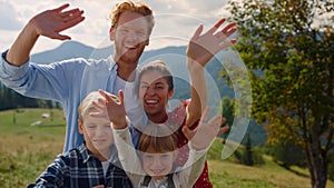 Cheerful family posing camera on green mountains. Parents have fun with kids.