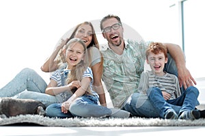 Cheerful family sitting on the carpet in the new living room