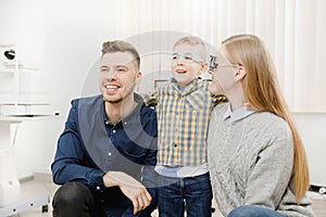 Cheerful family with small child reception doctor ophthalmologist using glasses