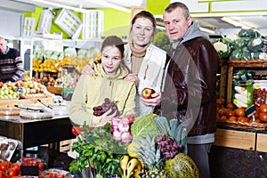 Cheerful family with small daughter standing near full grocery cart